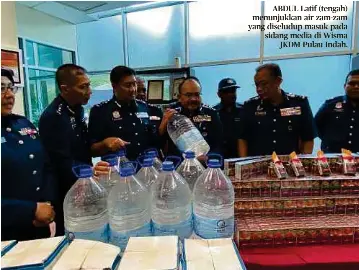  ??  ?? ABDUL Latif (tengah) menunjukka­n air zam-zam yang diseludup masuk pada sidang media di Wisma
JKDM Pulau Indah.