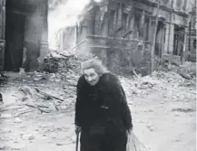  ??  ?? 0 An old woman passes burning buildings during Allied bombings on Berlin which began on this day in 1945
