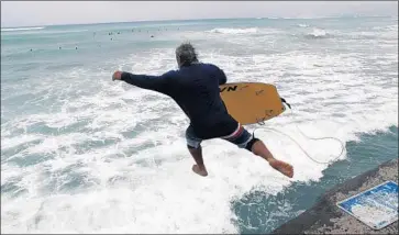  ?? John Locher Associated Press ?? A BODYBOARDE­R jumps into the surf at Waikiki Beach on Friday despite warnings to stay out of the water.