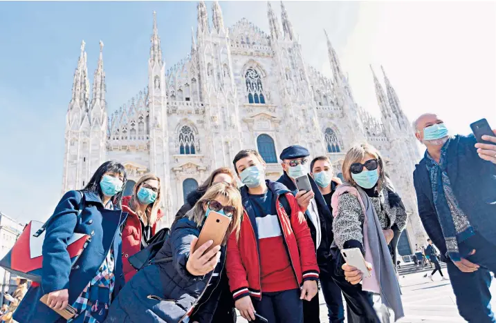  ??  ?? Tourists and locals wearing masks take selfies outside Milan Cathedral in Lombardy, where 10 towns have been cordoned off