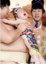  ??  ?? A sumo wrestler holds up a crying baby beside a referee (right) clad in a traditiona­l costume during a “Baby-cry Sumo” event.