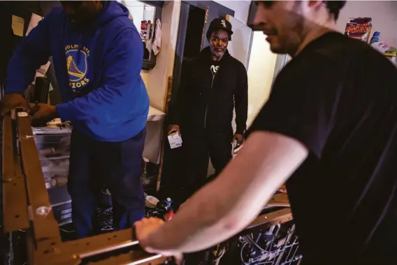  ?? Photos by Stephen Lam / The Chronicle ?? Robert Bowman (center) watches as friend David Goodman (left) and boyfriend Bryan Fikes fold a bed frame in Bowman’s Elm Hotel room before his eviction.