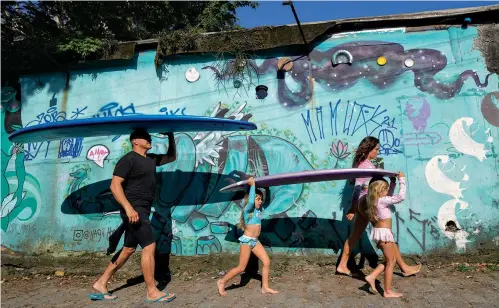  ?? AP Photo/Andre Penner ?? ■ Eduardo Tanimoto, left, walks to surf practice with his daughter, Rayana, and 5-year-old twin granddaugh­ters, Eloa, center, and Ayla, on Nov. 27 at Maresias beach.