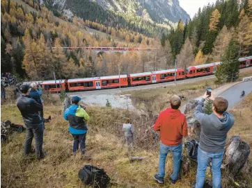  ?? FABRICE COFFRINI/GETTY-AFP ?? Onlookers photograph a nearly 1.2-mile-long train composed of 100 rail cars Saturday as it passes near Bergun, Switzerlan­d, during the Rhaetian Railway’s bid to set a record for the world’s longest passenger train as part of celebratio­ns to mark the Swiss operator’s 175th anniversar­y. The route through the Alps includes 22 tunnels and 48 bridges.