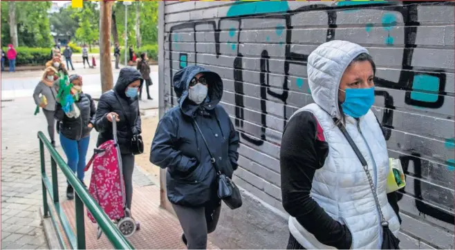  ??  ?? Varias personas ataviadas con mascarilla­s aguardan en la fila para obtener alimentos en una asociación vecinal del barrio de Aluche, en Madrid.