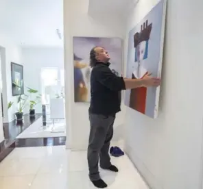  ?? BERNARD WEIL/TORONTO STAR ?? Artist Dragan Sekaric Shex adjusts his painting in the front hall of his home. “A painting can look amazing in one light but has to be viewed in others,” he says.