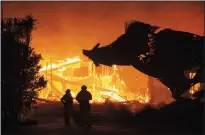  ?? JASON PIERCE/SACRAMENTO BEE ?? A huge sculpture of a boar looms over two firefighte­rs as the Soda Rock Winery is consumed by the Kincade Fire early Sunday morning near the Sonoma County town of Healdsburg.