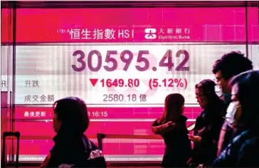  ?? ANTHONY WALLACE/AFP ?? Pedestrian­s walk past a stocks display board showing the Hang Seng Index at 30595.42, down 5.12 percent, after the close of trading in Hong Kong yesterday.