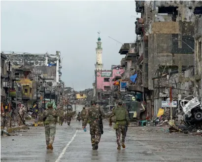  ?? AFP ?? Philippine soldiers walk past destroyed buildings in Bangolo district in Marawi on Tuesday. —