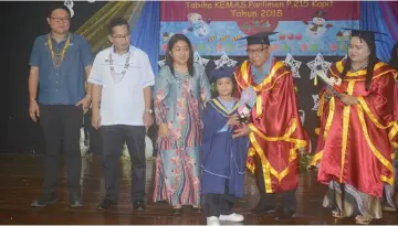  ??  ?? Joseph presents a scroll to a child during the ceremony, assisted by Leena (right) and witnessed by others.