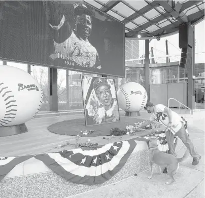  ?? JOHN BAZEMORE/AP ?? A man places flowers next to a portrait of Braves’ Hank Aaron on Friday outside Truist Park in Atlanta.