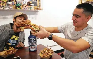  ?? Jerry Lara / Staff photograph­er ?? Isaac Sarabia, left, and his brother, Dominick Mata, toast with their sandwiches while eating at Smack’s Chicken Shack, where massive, crusty slabs of chicken comically overhang their buns.