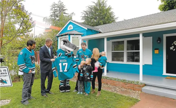  ?? DAN HONDA/STAFF PHOTOS ?? The Beech family, Vivan, 2, far right, Theresa, Evan, 7, Colin, 5, and Robert, are presented with gifts from Sharkie, Sharks' Executive Vice President, Chief Sales and Marketing Officer Flavil Hampsten and former Shark Dan Boyle in front of their newly...