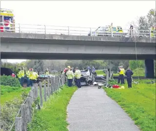  ??  ?? Emergency services at the scene of the crash; right, the crashed Mercedes is lifted off the footpath