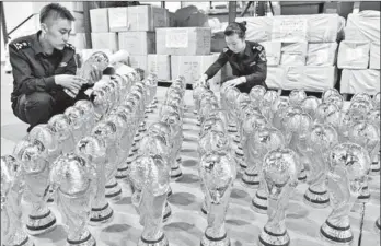  ?? LYU BIN / FOR CHINA DAILY ?? Customs officers check unauthoriz­ed World Cup trophies intercepte­d in Yiwu, Zhejiang province, on Wednesday.