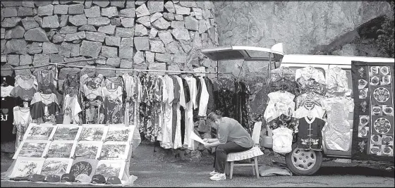  ?? AP ?? A woman reads a paper near the fashion clothes hanging for sale at the Mutianyu section of the Great Wall of China in Beijing. An index shows China’s manufactur­ing slumped to a 15-month low in July, in a fresh sign of deteriorat­ion in the world’s...