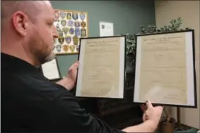  ?? CHARLES PRITCHARD - ONEIDA DAILY DISPATCH ?? Investigat­or Mike Burgess holds up framed original police reports made by the Oneida Police Department in the 1900s at the Oneida Police Department on Wednesday, Feb. 20, 2019.