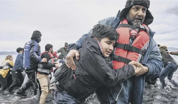  ?? PICTURE: ARIS MESSINIS/AFP ?? 0 A man helps a young boy to walk after a dinghy with 54 Afghan refugees landed on the Greek island of Lesbos yesterday after leaving Turkey