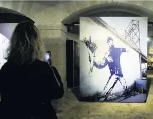  ??  ?? A woman takes a picture of Bansky’s Flower Thrower, seen here in a photograph­y exhibition in Porto
Farelight Production­s