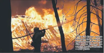  ??  ?? A Cal Fire fighter sprays water on a home next to a burning home as the Camp Fire moves through the area in Magalia, California. — AFP photo