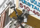  ??  ?? Surveillan­ce cameras are mounted to an overhead storefront sign in the Chinatown district of Oakland.