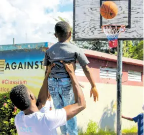  ?? ?? Volunteer Kimani Douglas lifts one of the children, lending a hand in the basketball shooting competitio­n.