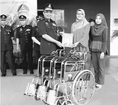  ??  ?? Shafien Mamat (centre) receives a bulletin and three wheelchair­s from Nur Shaqhiroh (second right). — Bernama photo