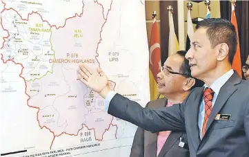  ??  ?? EC chairman Azhar (right) and Cameron Highlands district officer Datuk Ishak Md Napis look at a map of Cameron Highlands district after a press conference yesterday. — Bernama photo