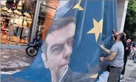  ?? Louisa Gouliamaki
AFP/Getty Images ?? PROTESTERS IN ATHENS last week take down a banner bearing an image of Greek Prime Minister Alexis Tsipras on a European Union f lag.