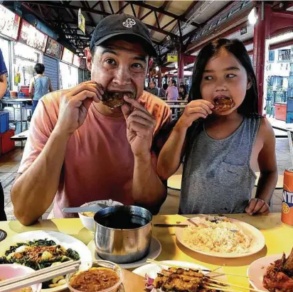  ?? Photos by Tessa Pierson photos / Los Angeles Times ?? David Pierson and daughter Ella try the fried chicken wings at Toa Payoh Lorong Food Center.