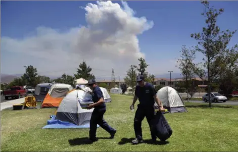  ?? NICK UT — THE ASSOCIATED PRESS ?? In this Tuesday photo, firefighte­rs carry food and supplies past dozens of firefighte­r tents covering a field at a firefighte­r operations base camp that has been establishe­d at Golden Valley High School in Santa Clarita as smoke from the Sand fire...