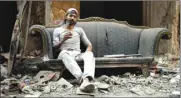  ??  ?? Abu Nimr, 36, smokes a cigarette as he sits on a sofa along a damaged street in Yarmouk Palestinia­n camp in Damascus.