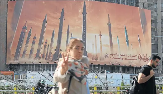  ?? MAJID ASGARIPOUR / REUTERS ?? Una mujer hace el gesto de la victoria en Teherán ante un gran cartel oficial presumiend­o de la potencia balística iraní.