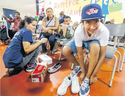  ?? JOHN MAHONEY ?? Carlos Del Valle tries on shoes Tuesday with his brother Rodrigo and mother Ann Lesly Altamirano and with help from volunteer Aura Perez, left, as Welcome Hall Mission gave out shoes and school supplies before the upcoming start of the school year.