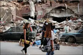  ?? (AP/Thibault Camus) ?? Women walk past destroyed vehicles Friday near the scene of Tuesday’s explosion in the Beirut seaport.