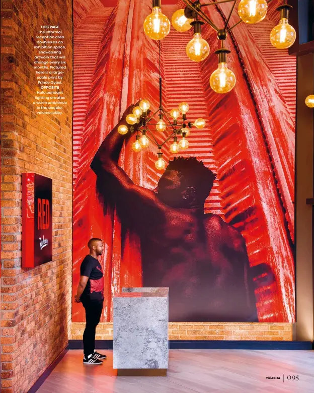  ??  ?? THIS PAGE
The informal reception area doubles as an exhibition space,
showcasing artwork that will change every six months. Pictured here is a largescale print by Prince Gyasi.
OPPOSITE Halo pendant lighting creates a warm ambience in the doublevolu­me lobby.