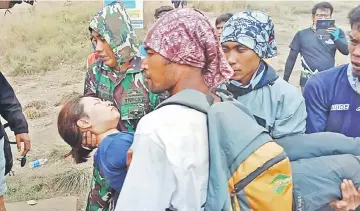  ?? — AFP photos ?? This handout picture released by the Indonesian military shows members of a search and rescue team helping a hiker (centre) as they decend from Mount Rinjani.