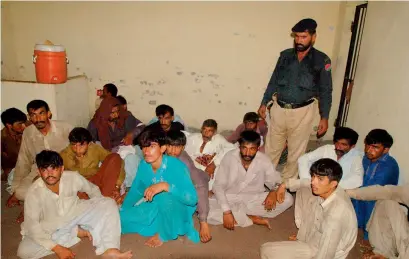  ?? AFP ?? A policeman stands guard near the arrested members of the village council in Raja Ram village on the outskirts of Multan. —