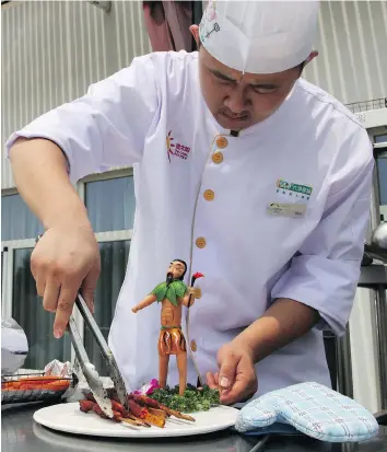  ??  ?? A chef sets a plate with food prepared in solar cookers near a mini statue of mythical Chinese archer Hou Yi, who shot down nine suns before harnessing fire for humanity’s benefit.