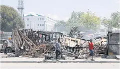  ?? REUTERS ?? People walk past remains of vehicles near the presidenti­al palace, after they were set on fire by gangs, in Port-au-Prince on March 25.