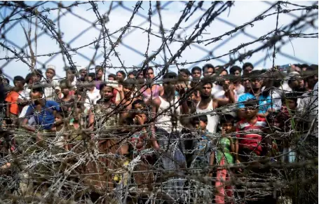  ??  ?? Photo ci-dessus : Le 25 avril 2018, des réfugiés rohingya se rassemblen­t derrière une clôture de barbelés dans un campement temporaire construit dans le no man’s land frontalier entre la Birmanie et le Bangladesh. Les deux pays ont signé en janvier dernier un accord prévoyant un retour échelonné sur deux ans des réfugiés de cette minorité musulmane dans l’État Rakhine. (© AFP/ Ye Aung Thu)