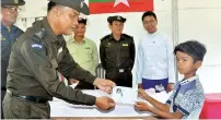  ??  ?? A Myanmar official handing over identifica­tion documents to a boy who belonging to the five-member Rohingya family, in Maungdaw. — AFP
