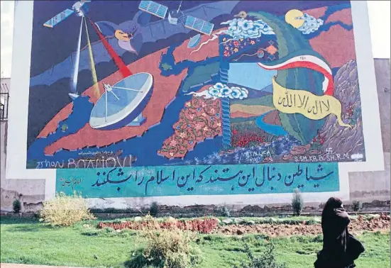  ?? KAVEH KAZEMI / GETTY ?? Una mujer pasa en Teherán junto a un mural en que se representa a las cadenas vía satélite como demoniacas y enemigas del islam