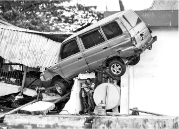  ??  ?? A survivor walks under a car struck on a building in Palu. — AFP photo