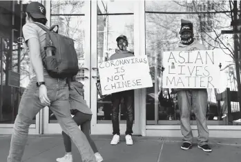  ?? MICHAEL M. SANTIAGO/GETTY ?? Cameron Hunt and his father, Calvin Hunt, hold signs of support as they stand Tuesday near the spot where an Asian American woman was attacked Monday in New York City. The NYPD is calling the attack a hate crime.