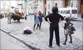  ??  ?? In this file photo, a woman poses with the Fearless Girl statue in New York. Since 1989 the bronze bull (left), has stood in New York City’s financial district as an image of the might and hard-charging spirit of Wall Street. But the installati­on of...