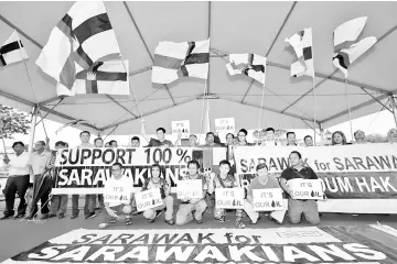  ??  ?? Demonstrat­ors in Kuching hold up flags and banners.