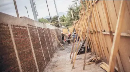  ??  ?? ► Un grupo de obreros estuca el nuevo muro de Pinto Durán, tras un panel de madera.