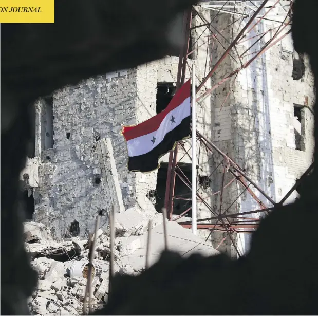  ?? MOHAMAD ABAZEED / AFP / GETTY IMAGES ?? The Syrian national flag stands amid shattered buildings in Daraa-al-Balad on Thursday after Syria’s army entered the area, the cradle of the uprising that sparked the country’s seven-year war, following a deal for rebels to hand over their heavy weapons.
