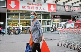  ?? (AFP) ?? A woman wearing a face mask walks out the Auchan supermarke­t in Beijing on Monday